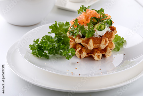 Belgian waffles with red fish and greens on a white dish on a white background