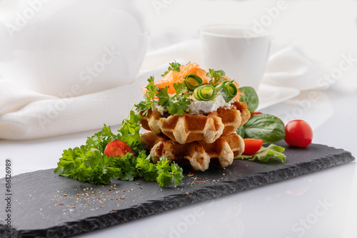 Belgian waffles with greens and red fish on a black plate on a white background