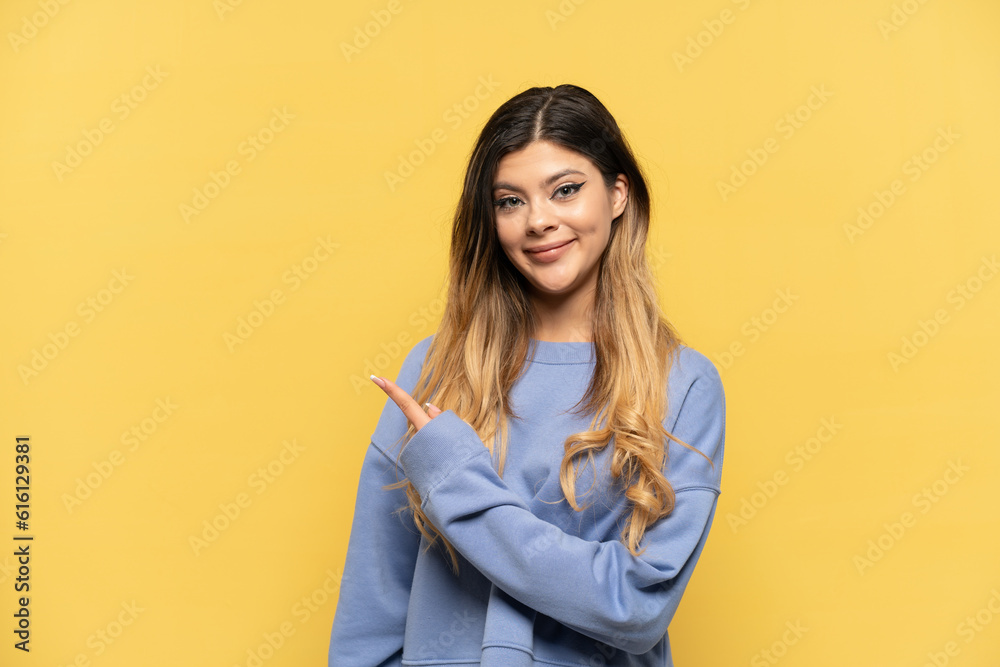 Young Russian girl isolated on yellow background pointing to the side to present a product Young Russian girl isolated on yellow background pointing to the side to present a product