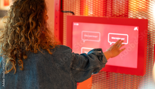 Curly hair woman using touch screen at the science exhibition. Taking interactive quiz in modern art museum or buying reservation tickets.