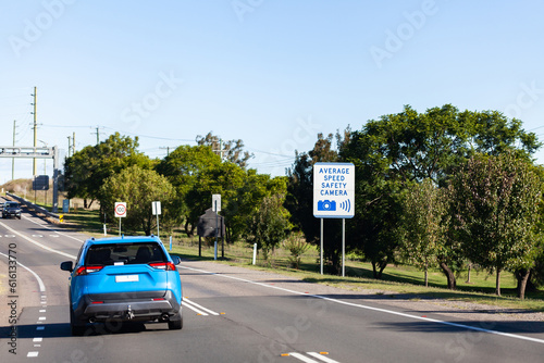 Blue car on road driving past average speed camera warning sign