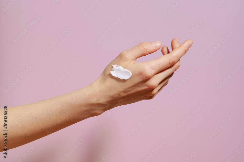 Fragile female hand with white cream smear on purple isolated background. Concept of cosmetics for moisturizing and face care, cream sample