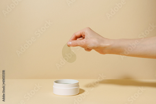 Foto Female hand holding sample of green algae extract eye patch over white jar of product on beige isolated background