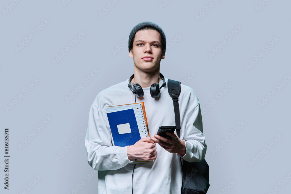 Young serious male student with headphones books using smartphone, on grey background Young serious male student with headphones books using smartphone, on grey background