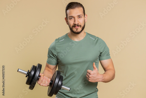 Like. Athlete sportive man raises thumbs up agrees with something or gives positive reply feedback recommends advertisement likes good. Middle eastern sportsman guy with dumbbell on beige background