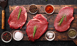 Raw meat on a rustic table with assorted spices on a dark background. Topview.