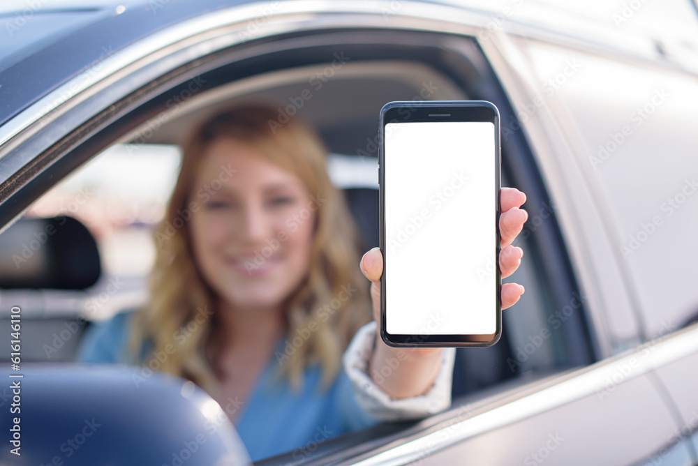 Attractive woman showing smartphone out the window of a car.