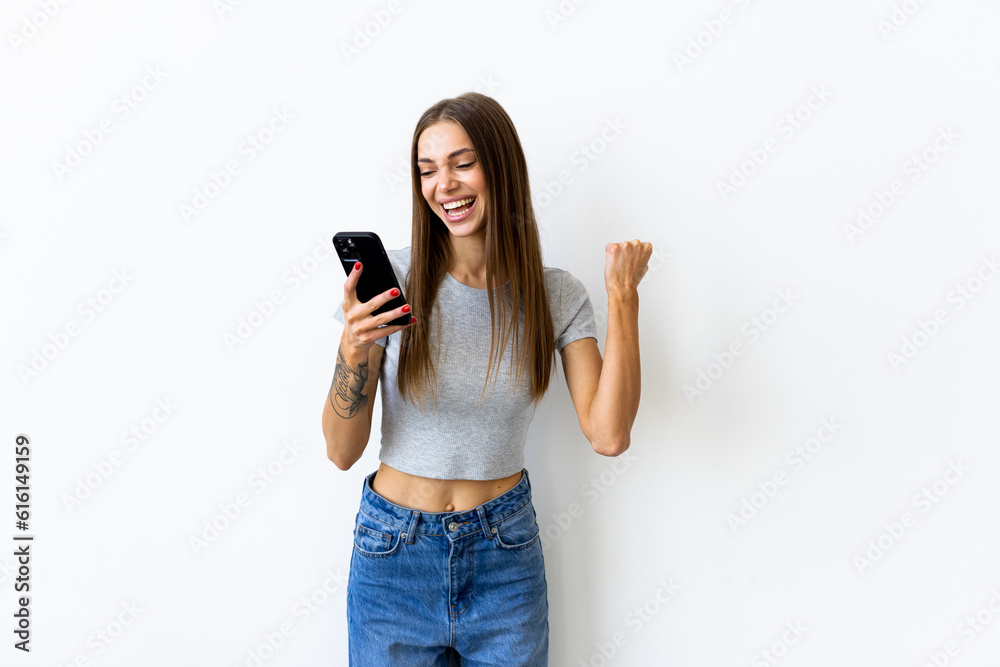 Portrait of a woman holding mobile phone and celebrating a win isolated over white background Portrait of a woman holding mobile phone and celebrating a win isolated over white background