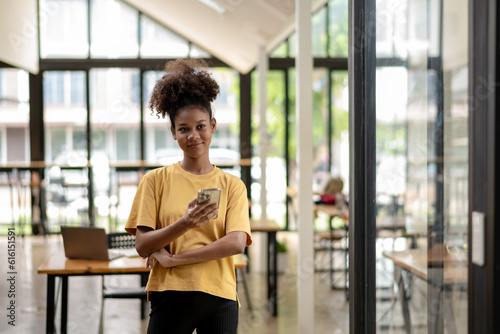 Smiling African American businesswoman, Freelance business woman in casual look standing in coworks space and cafe, using mobile phone. © Wasana