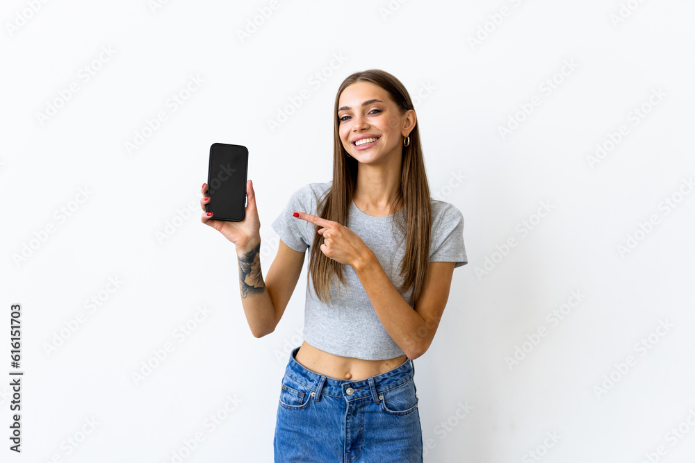 Smiling woman pointing on smartphone standing on white background. Smiling woman pointing on smartphone standing on white background.