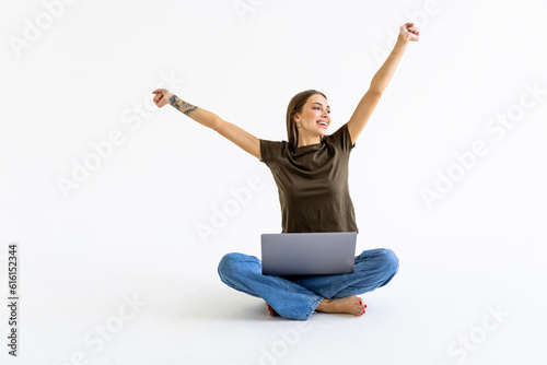 Beautiful woman with arms up sitting with crossed legs and working with a laptop