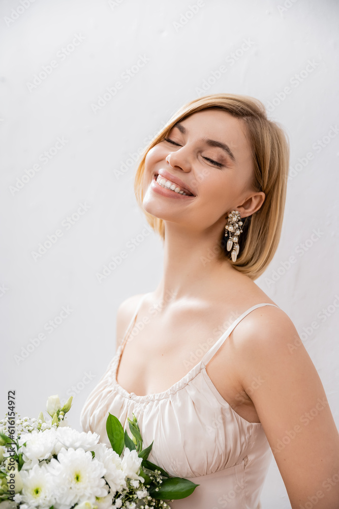beautiful and blonde bride in wedding dress holding bouquet on grey background, joy, white flowers, bridal accessories, happiness, special occasion, feminine, blissful beautiful and blonde bride in wedding dress holding bouquet on grey background, joy, white flowers, bridal accessories, happiness, special occasion, feminine, blissful