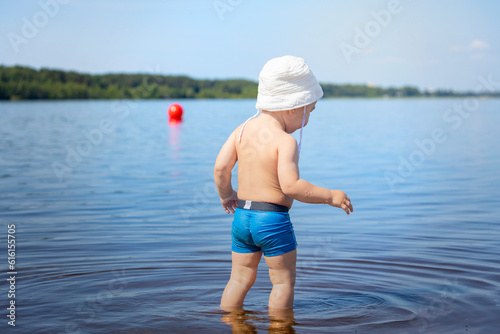 .baby 1 year old on the beach, a child in swimming trunks and a hat is going to swim