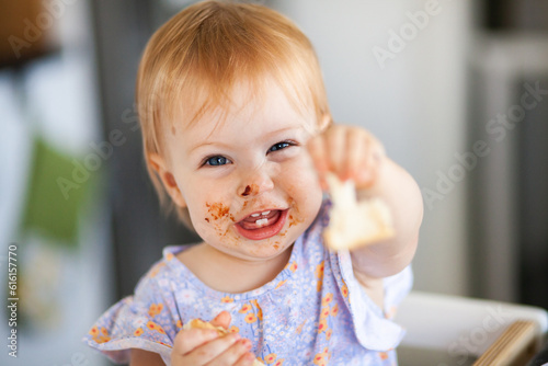 One year old baby with messy face holding out piece of toast to share photo