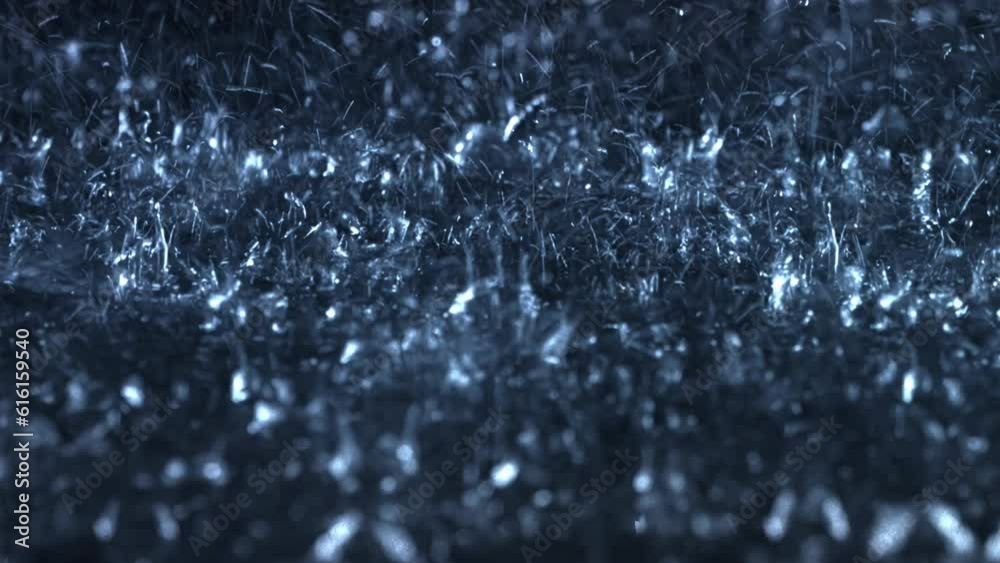Heavy rain falls in front of the camera against black screen. Raindrops are splashing. Rain closeup VFX insert. Practical, seamlessly loopable footage. Heavy rainstorm hitting black surface.	