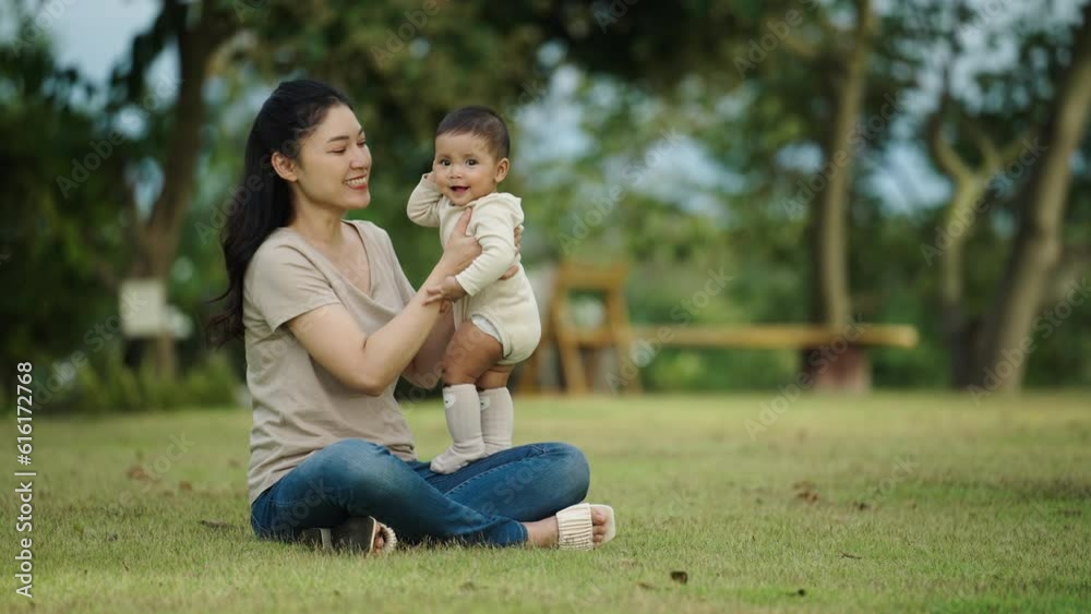 mother talking and playing with her infant baby while sitting on a grass field mother talking and playing with her infant baby while sitting on a grass field