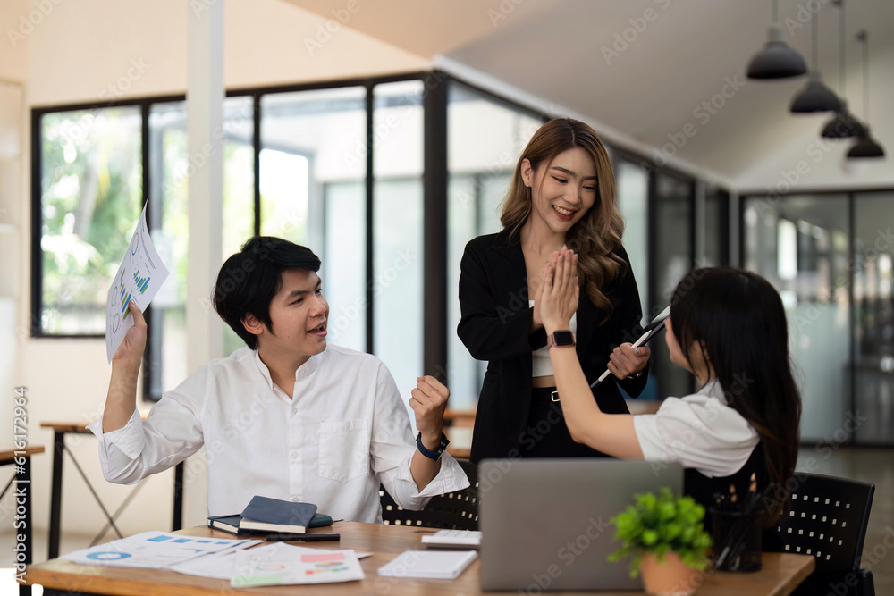 Successful business people giving each other a high five in a meeting. Three young business celebrating teamwork in an office