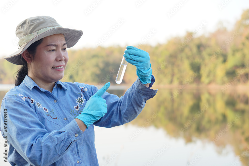 Asian woman environment researcher holds tube of sample water to inspect from the lake. Concept, explore, analysis water quality from natural source. Ecology field research. Asian woman environment researcher holds tube of sample water to inspect from the lake. Concept, explore, analysis water quality from natural source. Ecology field research.
