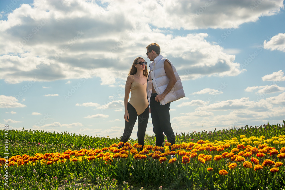 A beautiful young couple, fashion models stands in sportswear at the background of a field of colorful tulips.