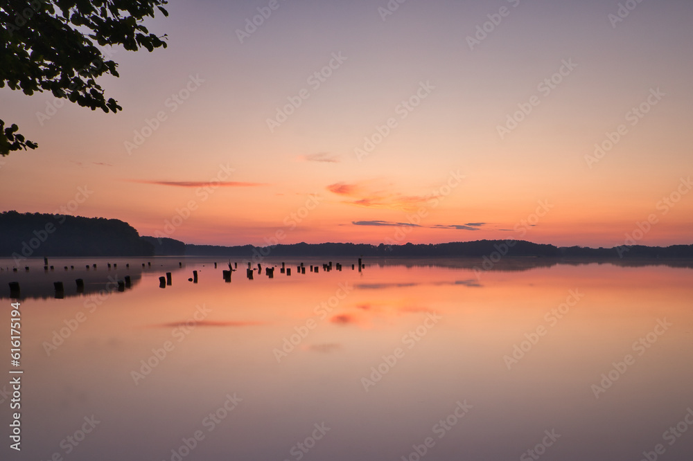 Fototapeta premium See im Abendrot - Sunset - Landscape - Beautiful Sunset scene over the lake and silhouette hills in the background - Sunrise over sea - Colorful - Reed - Clouds - Sky - Sundown - Sun 