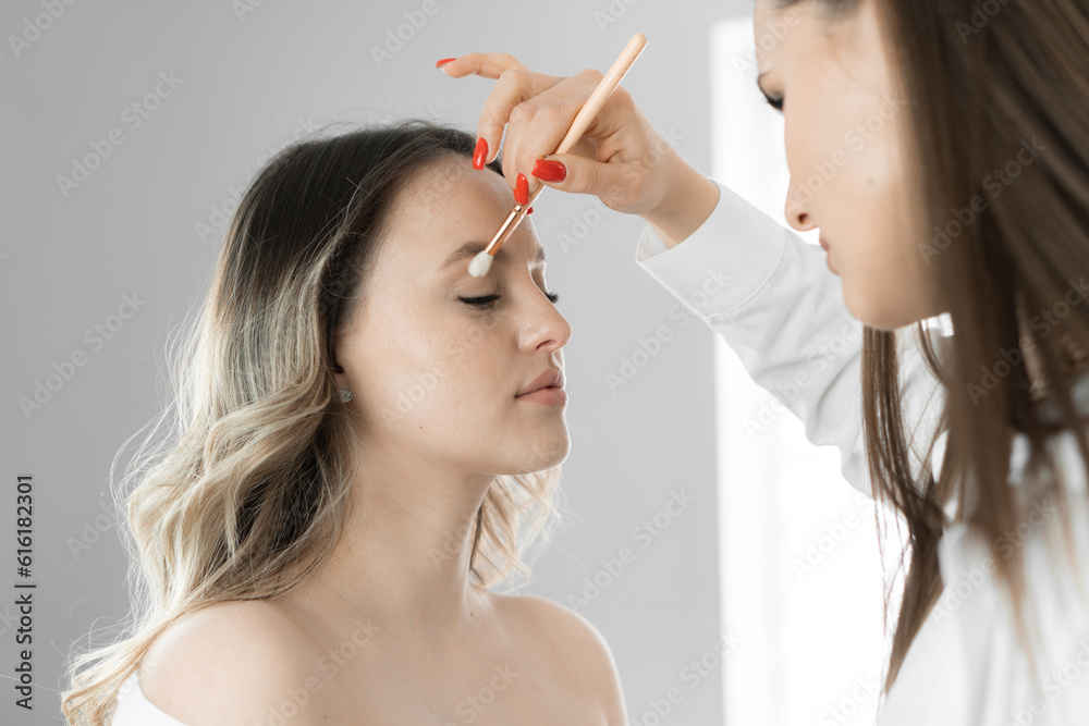 Obraz premium Reflecting the shades of modern fashion, the makeup artist applies a natural tone of makeup to a young woman's face, creating a reprimandable base that emphasizes her natural beauty in a beauty studio