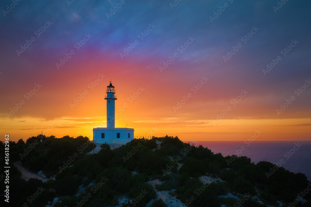 Captivating sunset over the  white lighthouse perched on Cape Ducato, Lefkada, Greece. Majestic lighthouse atop a cliff, with the sun gently caressing the sea in the backdrop