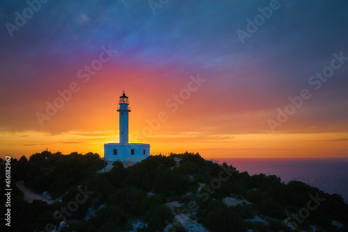 Captivating sunset over the white lighthouse perched on Cape Ducato, Lefkada, Greece. Majestic lighthouse atop a cliff, with the sun gently caressing the sea in the backdrop
