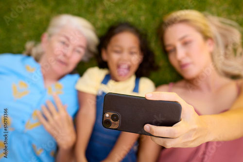 Overhead Shot Of Multi-Generation Female Family Lying On Grass Taking Selfie On Mobile Phone