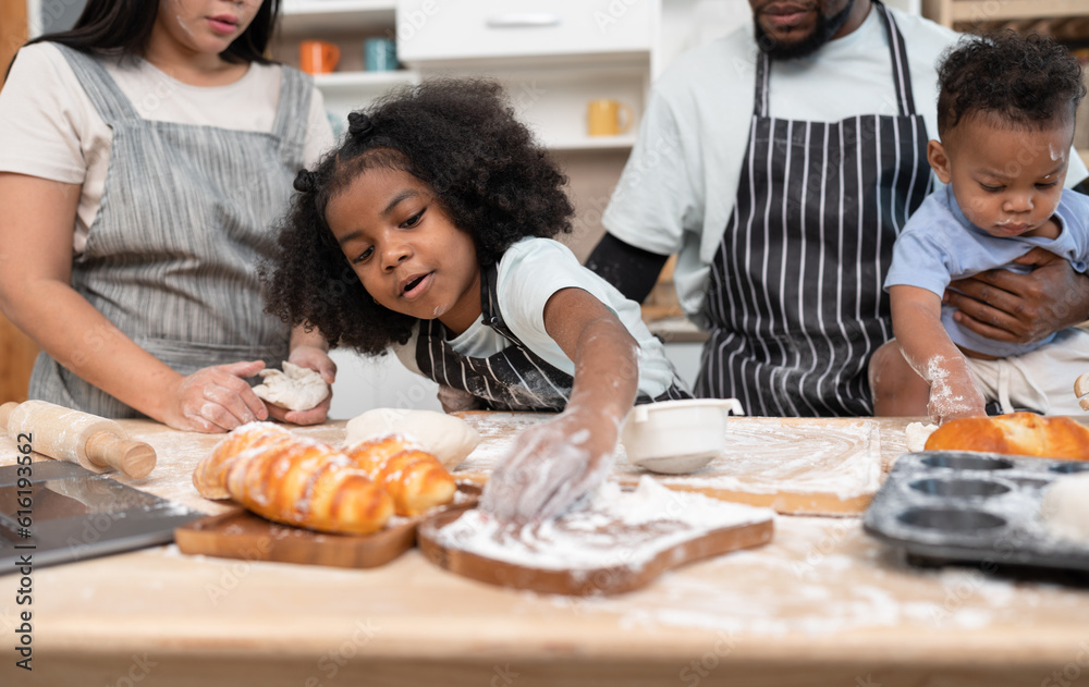 Happy African American kid girl with family cooking break or bakery at kitchen at home	