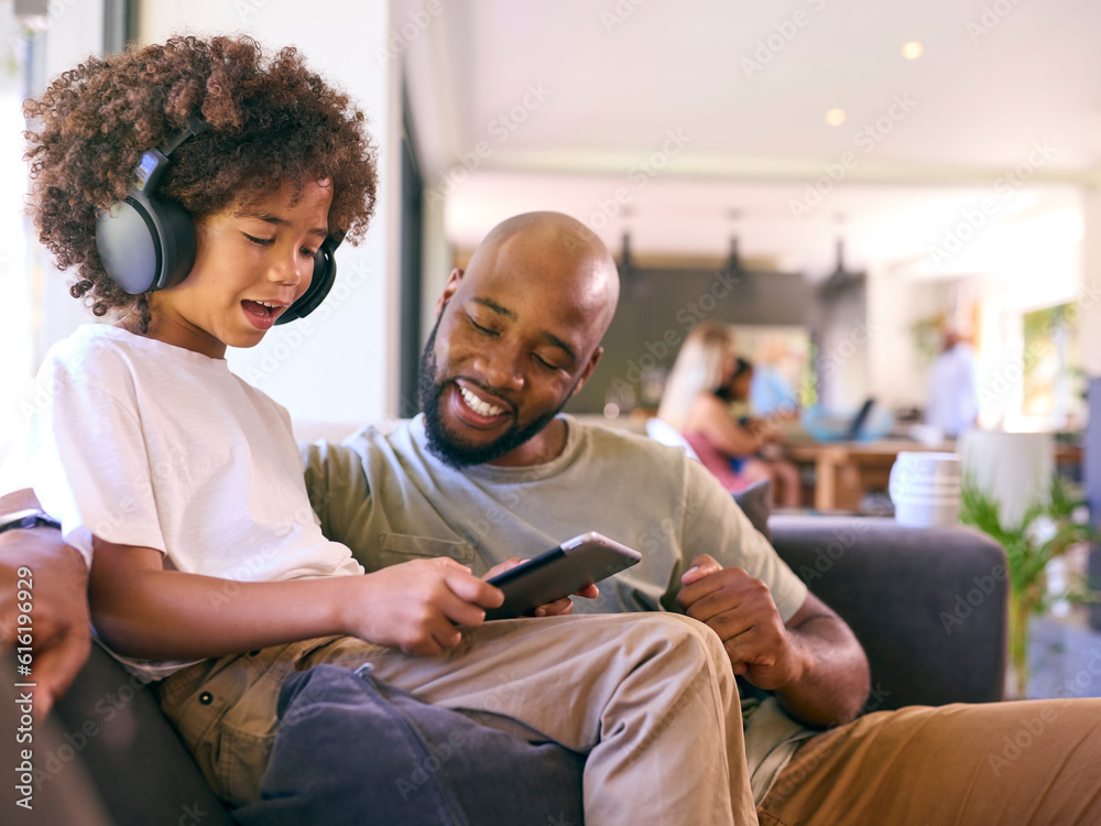 Obraz premium Father And Son Using Digital Tablet With Headphones At Home With Multi-Generation Family Behind