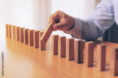 Foto Wooden game strategy, Businessman hand stopping falling wooden dominoes effect from continuous toppled or risk, strategy and successful intervention concept for business