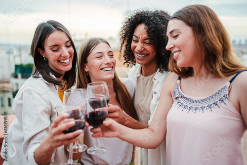 Fotografia Group of happy young women friends having fun toasting wine glasses on a rooftop party, drinking and laughing together