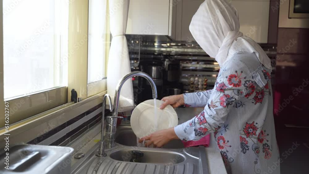 Middleaged muslim woman does housework Kitchen cleaning sink wearing