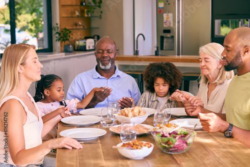 Multi-Generation Family Holding Hands And Saying Prayer Before Meal At Home 