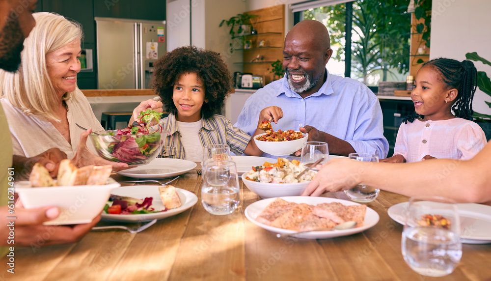 Multi-Generation Family Sitting Around Table Serving Food For Meal At Home 