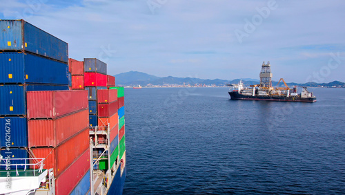 View on large offshore drill ship from ultra large container ship with loaded containers on board.