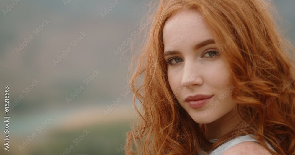 Close up shot of face of beautiful young caucasian girl with red hair and freckles looking at camera and positively smiling. Cute woman on portrait in nature. Copy Space Close up shot of face of beautiful young caucasian girl with red hair and freckles looking at camera and positively smiling. Cute woman on portrait in nature. Copy Space
