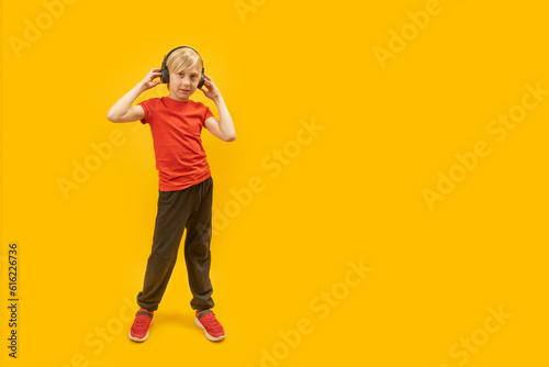 Fototapeta Naklejka Na Ścianę i Meble -  Full-length portrait of teenage boy in sportswear with headphones on his head in isolation on yellow background. Copy space.