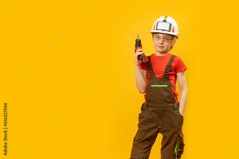 Portrait of boy in work overalls and helmet with drill in his hands. Role of construction worker. Copy space, mockup. Choice of profession.