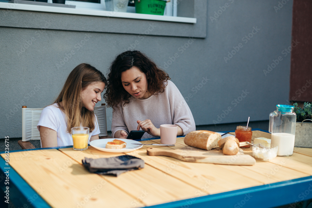 Mother and daughter using technology during breakfast in the garden. Mother and daughter using technology during breakfast in the garden.