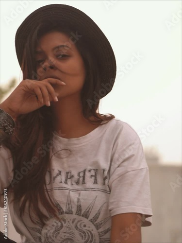 A girl is sitting on rooftop wearing hat and feeling the fresh air, waving the hair