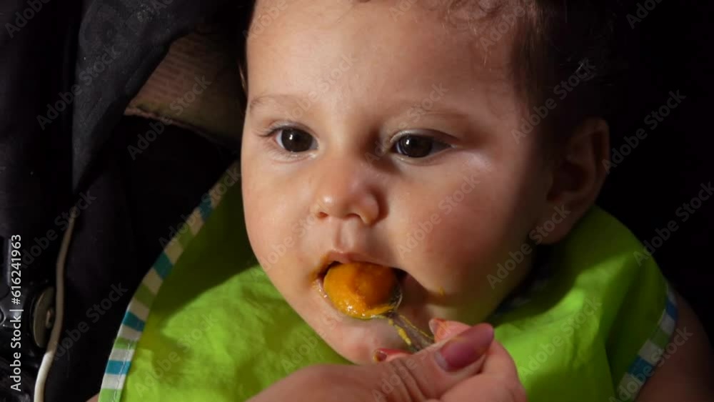 Close-up of the curly brown-eyed hungry baby boy eats mashed carrot Close-up of the curly brown-eyed hungry baby boy eats mashed carrot