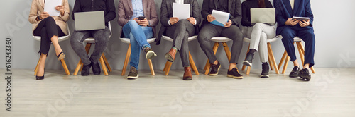 Tela Legs of unrecognizable business people sitting on the chairs in a row with resumes and laptops in their hands