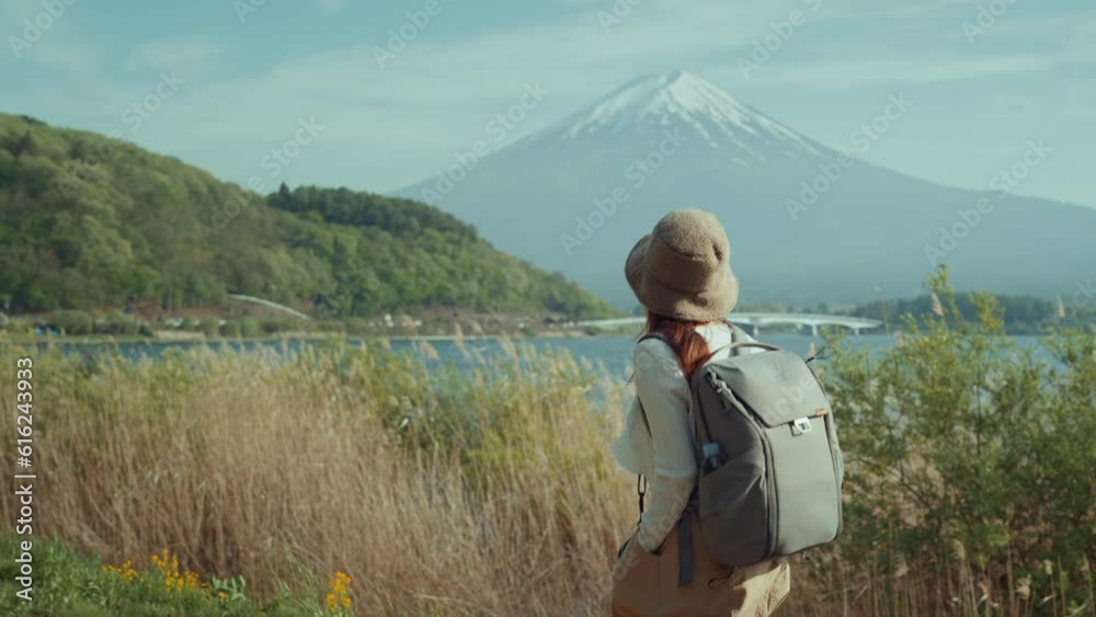 Side view of woman traveler walking by the lake Kawaguchi and looking at mountain Fuji view in bright day, Japan travel vacation, Freedom