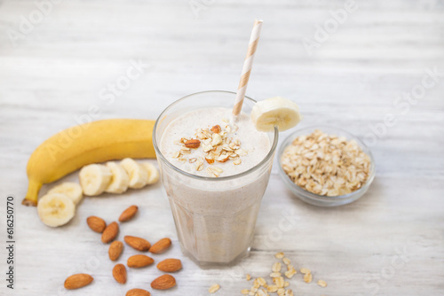 Banana smoothie with oat flakes and almond in glass. Healthy food. White wooden background. Copy space. 