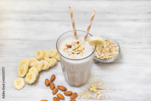 Banana smoothie with oat flakes and almond in glass. Healthy food. White wooden background. Copy space. 