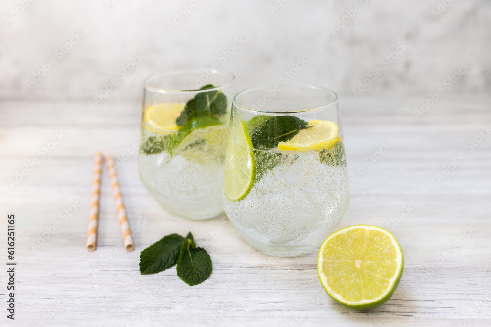 Cold refreshing lemonade drink or cocktail made of sparkling water, citrus and mint. Served drinking glass with ice cubes. On white wooden backgrond with copy space. Cold refreshing lemonade drink or cocktail made of sparkling water, citrus and mint. Served drinking glass with ice cubes. On white wooden backgrond with copy space.
