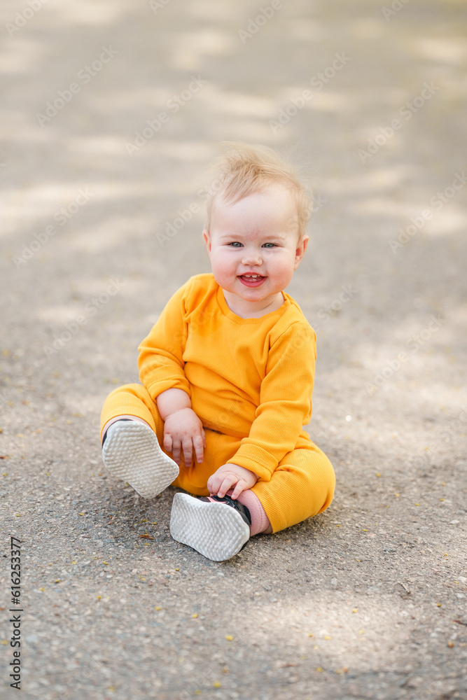 Funny kid toddler is sitting on the asphalt in a yellow suit