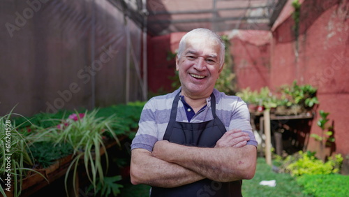 Friendly happy senior older horticulturist with arms crossed smiling at camera in Plant backyard environment