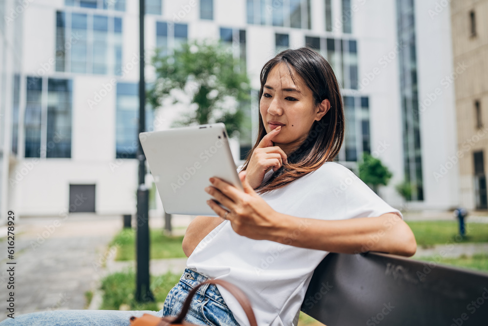 Fototapeta premium Young Japanese Business woman sitting in the street using a tablet and reading something